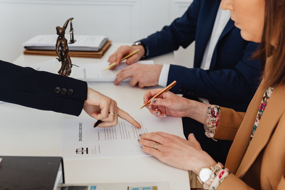 Two people reviewing and pointing at a settlement agreement on a desk beside scales of justice