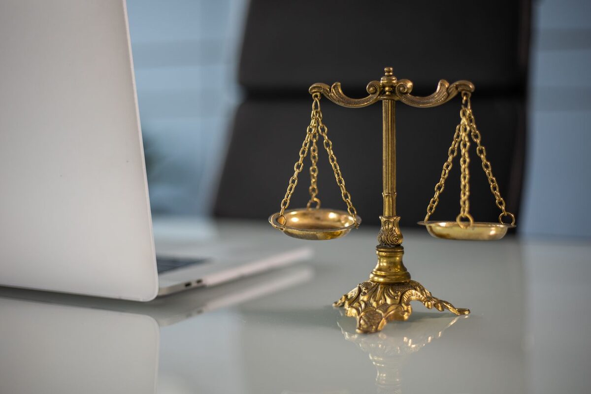 Brass scales of justice on a desk beside a laptop - civil complaint and lawsuit document preparation